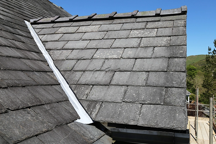 Close-up of a pitched roof with overlapping gray slate tiles and a metal flashing joint.