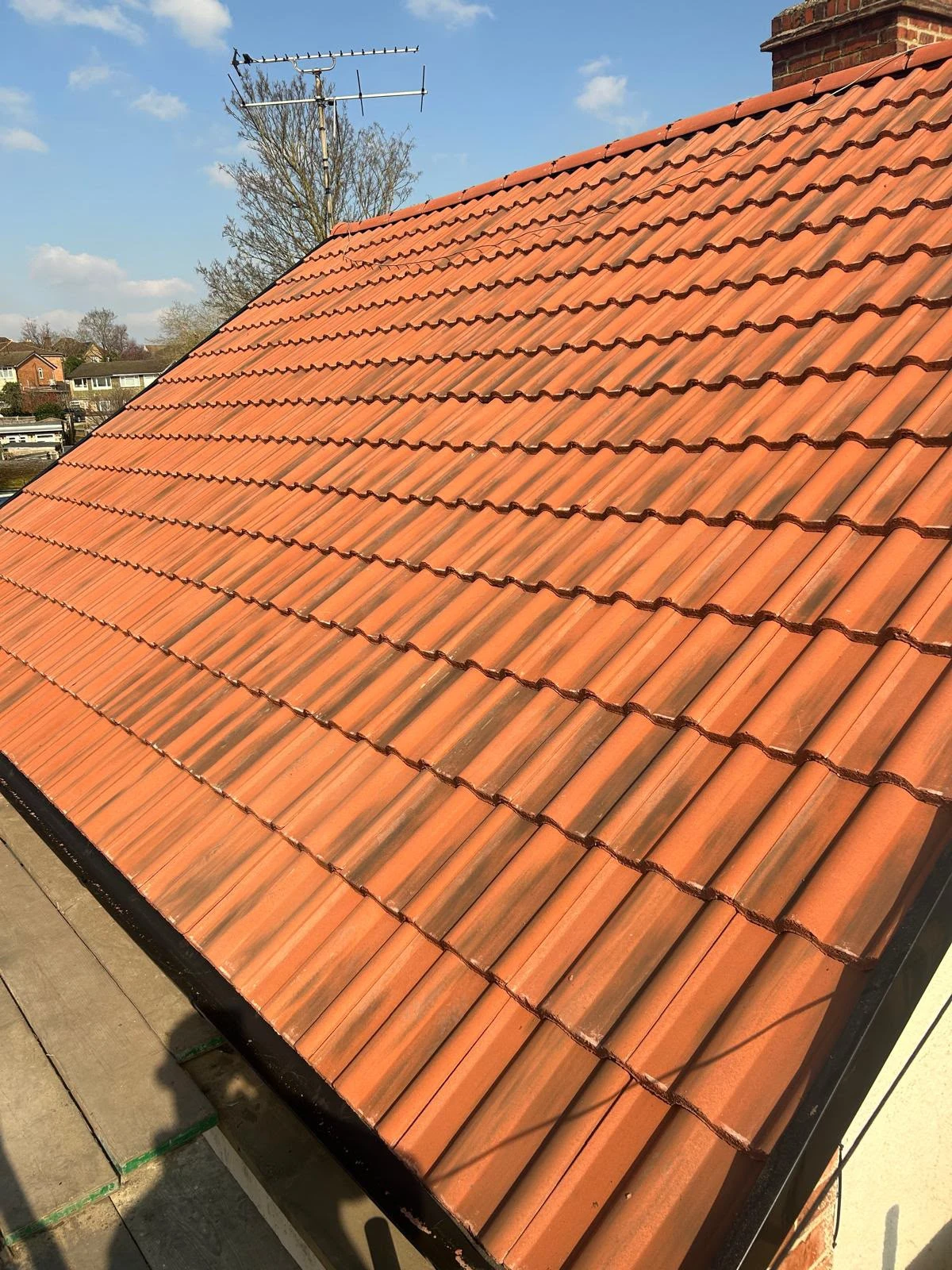 Orange tiled roof with an antenna against a blue sky and some trees in the background.