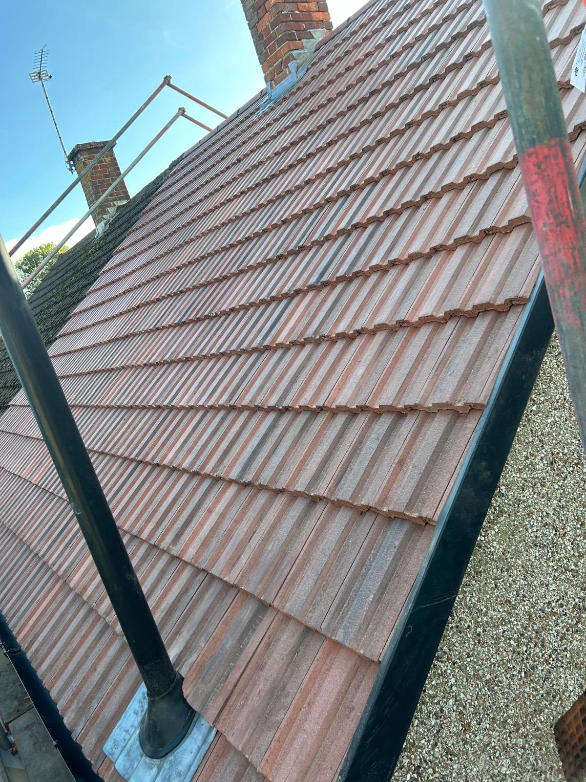 New reddish-brown roof tiles arranged in neat rows on a slanting roof during daytime.