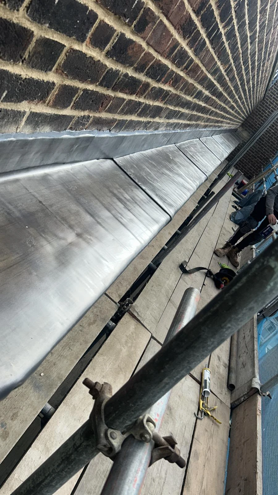 Construction scaffolding platform with metal flashing attached to a brick wall and a worker standing.